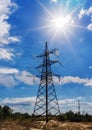 High voltage electricity pylons against blue sky and sun rays. Royalty Free Stock Photo