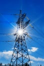 High-voltage electricity pylons against blue sky and sun rays Royalty Free Stock Photo