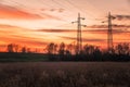 High voltage electricity pylons in a field and orange sky at sunset Royalty Free Stock Photo