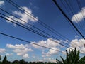 High voltage line wires and pole against beautiful blue cloudy sky passing banana trees and leaf Royalty Free Stock Photo