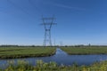 High voltage lines and power pylons in a flat and green agricultural landscape on a sunny day with cirrus clouds in the blue sky Royalty Free Stock Photo