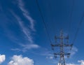 High-voltage pole against a blue sky with beautiful white clouds. Overhead power line wires. Bottom view Royalty Free Stock Photo