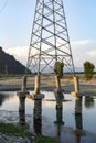 High voltage post in the river water after a heavy flood in the area erode the soil form the pillars