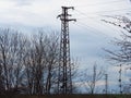 High voltage power lines against gloomy blue sky and leafless trees. Old system electric power grid view. Electric pillars poles. Royalty Free Stock Photo