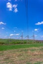 High-voltage power lines in green field against blue sky with white clouds. Royalty Free Stock Photo