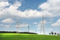 High-voltage power lines in green field against blue sky with white clouds. Power line in green meadow.