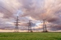 High-voltage power lines passing through a green field, on the background of a beautiful cloudy sky Royalty Free Stock Photo