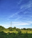 High voltage pylons and lines in a rural landscape against a blue sky. green country landscape on a sunny day. Royalty Free Stock Photo