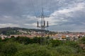 High-voltage tower against a cloudy sky. An electric line in the forest against the background of the city. Royalty Free Stock Photo