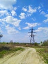 High-voltage tower of a line of air transmission of electric energy in a field against a blue cloudy sky, dirt road