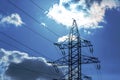 High voltage tower with power wires against the background of the sun, sky and clouds. The concept of a source of electricity.