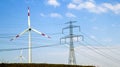 High voltage tower and wind turbines against blue sky