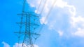 High voltage transmission tower with cable lines against clouds on blue sky background, low angle and widescreen view Royalty Free Stock Photo