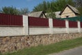 High wall fence made of brown stones white bricks and red metal