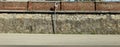 High wall made of stones in the lower side and bricks in the upper. A convex mirror on a road pole and asphalt street in front.