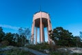 High water tower stands in the forest at the top of the mountain. Huge building structure made of white concrete. Bottom view.