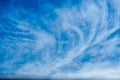 High white wispy cirrus clouds expanding by wind to cover deep navy blue sky in summer sunny day.