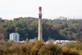 High wide concrete red and white rectangle industrial chimney rising high above industrial complex with new storage tanks Royalty Free Stock Photo