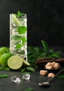 Highball glass of Mojito cocktail with ice cubes,mint and lime on black board with spoon and wooden squeezer and fresh limes with Royalty Free Stock Photo