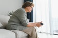 A highly emotional older lady sits on the couch at home and plays video games. Grandma wins while sitting alone at home.