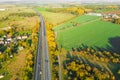 Highway between Autumn forest and cultivated ground with yellow trees at sunset in autumn. Aerial view of the traffic on speedway.