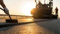 Highway construction workers applying asphalt on a new road surface during sunset, showcasing teamwork and machinery in action Royalty Free Stock Photo