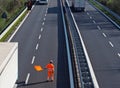 A highway worker with a high visibility work suit waves the orange flag to slow down trucks traffic before the roadblock Royalty Free Stock Photo