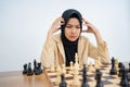 Hijab woman thinking looking at chess pieces while playing chess