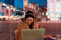 A hijab woman using laptop and smartphone at a modern coffe in the nighttime cityscape, reflecting the harmonious blend