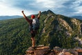 Hiker with arms up standing on the top of the mountain. A man with a backpack in the mountains at sunset, rear view.