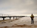 Hiker with backpack alone on sandy beach, sunrise above sea bridge. Royalty Free Stock Photo