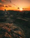 Hiker with backpack sitting on mountain and enjoying sunset