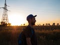 Hiker with backpack standing on a hill and enjoying sunset. Bearded man in snapback walking. Local travel nature concept Royalty Free Stock Photo