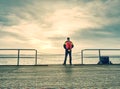 Hiker with the backpack walk over the wood pier on shore of river. Fall moody atmosphere at river Royalty Free Stock Photo