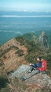 Hiker with backpacks reaches the summit of mountain peak. Female traveler on high top of rock enjoying wild environment landscape.