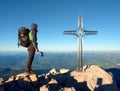 Hiker at big crucifix on mountain peak. Iron cross at Alps mountain top. Royalty Free Stock Photo
