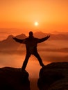 Hiker in black celebrate triumph between two rocky peaks. Wonderful daybreak in rocky mountains, heavy orange mist in deep