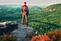 Hiker in black with red baseball cap on sharp cliff and watch to valley. Colorful summer day. Royalty Free Stock Photo