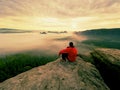 Hiker in black on the rocky peak. Wonderful daybreak in mountains, heavy orange mist in deep valley.