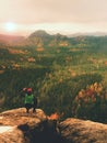 Hiker with camera on tripod takes picture from rocky summit. Alone photographer at edge photograph landscape