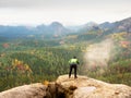 Hiker with camera on tripod takes picture from rocky summit. Alone photographer at edge photograph landscape