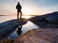 Hiker in dark sportswear with poles and sporty backpack. Coastline trail on rocky shore. Alone tourist enjoy Royalty Free Stock Photo