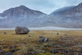 Hiker dwarfed by a big rock in remote arctic valley on a cloudy, rainy day. Dramatic arctic landscape of Akshayuk Pass