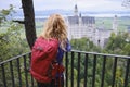 Hiker girl with backpack looks towards Neuschwanstein castle, in Bavaria, Germany from a viewpoint above. Tourism. Royalty Free Stock Photo