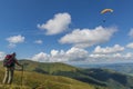 Hiker girl on the mountain top looks at the blue sky with soaring paraglider wing