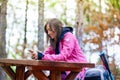 Hiker girl resting on a bench in the forest. Backpacker with pink jacket holding cell phone