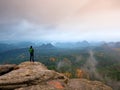 Hiker in green windcheater, cap and dark trekking trousers stand on mountain peak rock. Royalty Free Stock Photo