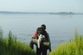 Hiker with her sleeping pad and backpack on, standing on the grassy shore, looking out over the sea