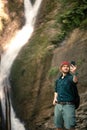 Hiker holds smartphone trying to find connection in deep forest with waterfalls. Royalty Free Stock Photo