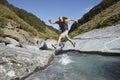 Hiker Jumping Across Forest River